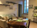 Accogliente spazio open space rustico che unisce una zona pranzo con tavolo in legno apparecchiato e un soggiorno con divano confortevole sotto travi a vista. Vista su finestra e mobile in ferro battuto. Catina Basi