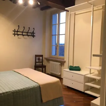 Camera da letto accogliente che unisce il fascino rustico delle travi a vista e del pavimento in legno con un design moderno, scaffalature aperte e un tocco di ferro battuto. Catina Basi