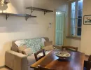 Accogliente zona giorno open-space con soffitto a travi a vista, tavolo da pranzo in legno massiccio, divano invitante e scaffali decorativi. Stile rustico e confortevole. Catina Basi