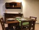 Sala da pranzo rustica e accogliente con un tavolo in legno massiccio apparecchiato con piatti colorati e vivaci. Una credenza coordinata e una caratteristica testa di moro ceramica decorano lo sfondo. Catina Basi