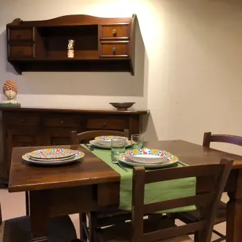 Sala da pranzo rustica e accogliente con un tavolo in legno massiccio apparecchiato con piatti colorati e vivaci. Una credenza coordinata e una caratteristica testa di moro ceramica decorano lo sfondo. Catina Basi