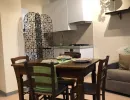 Open space rustico e accogliente con travi a vista, tavolo in legno massiccio apparecchiato, cucina moderna e un caratteristico divisorio in ferro battuto. Catina Basi