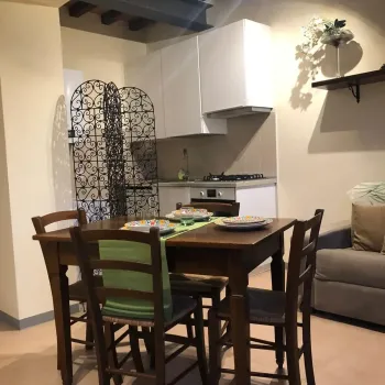 Open space rustico e accogliente con travi a vista, tavolo in legno massiccio apparecchiato, cucina moderna e un caratteristico divisorio in ferro battuto. Catina Basi