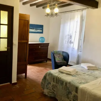 Accogliente camera da letto in stile rustico con pavimento in cotto e travi a vista. Arredata con letto matrimoniale, antico com&ograve; in legno e dettagli azzurri. Catina Basi