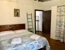 Camera da letto rustica con travi a vista e pavimento in cotto. Presenta un letto con testiera in legno, copriletto azzurro e una scala a pioli decorativa. Catina Basi