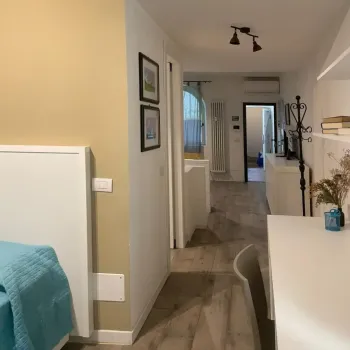 Luminoso appartamento dal design moderno. Vista su un accogliente corridoio con pavimento effetto legno, angolo studio e camera con vivace copriletto azzurro. Catina Basi