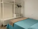 Camera da letto moderna e luminosa dal design minimalista. Presenta un letto matrimoniale con copriletto azzurro e un pratico guardaroba aperto bianco. Catina Basi
