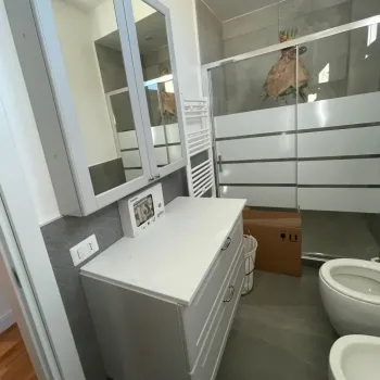 Bagno moderno caratterizzato da un elegante mobile lavabo sospeso bianco con ampi cassetti e specchiera contenitore coordinata. Catina Basi