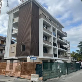 Edificio residenziale multipiano di moderna concezione caratterizzato da ampi balconi con parapetti in vetro scuro e rivestimenti verticali a effetto legno su una porzione della facciata